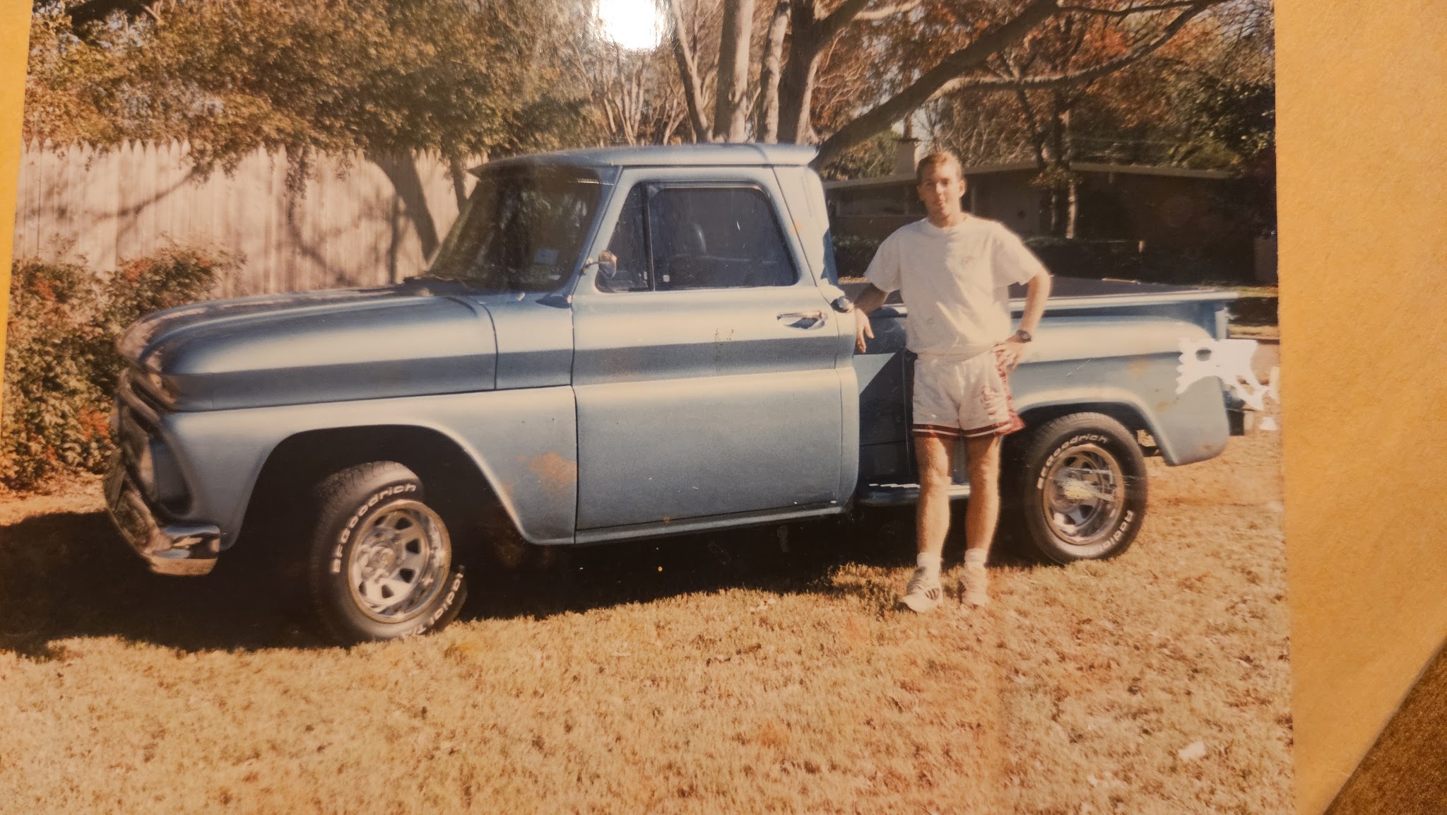 1966 Chevy C10 stepside pickup in faded light blue paint parked on a lawn with a person standing beside it, from an old print photo